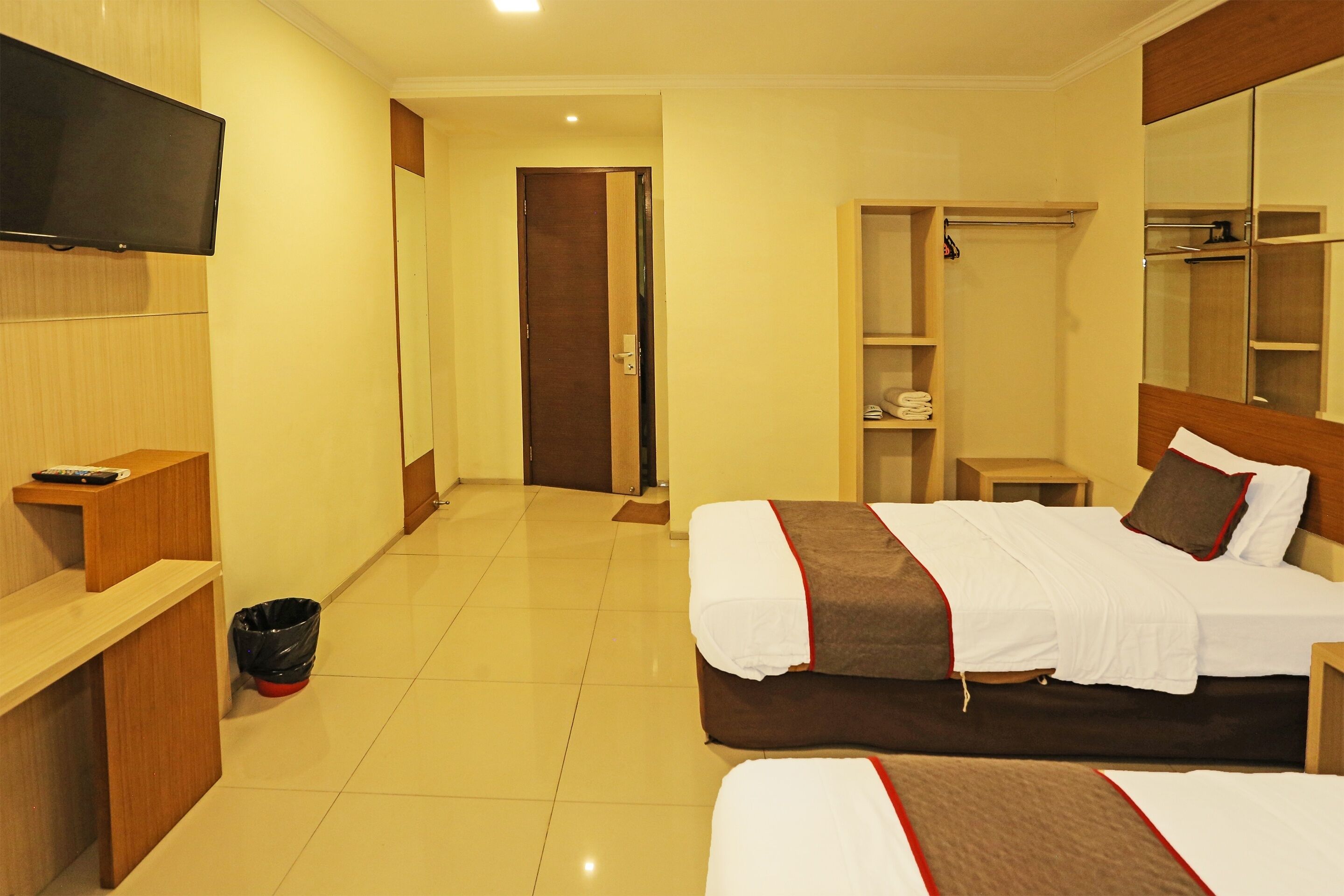 A hotel room with a bed, a TV mounted on the wall, a wooden wardrobe, and a small table.