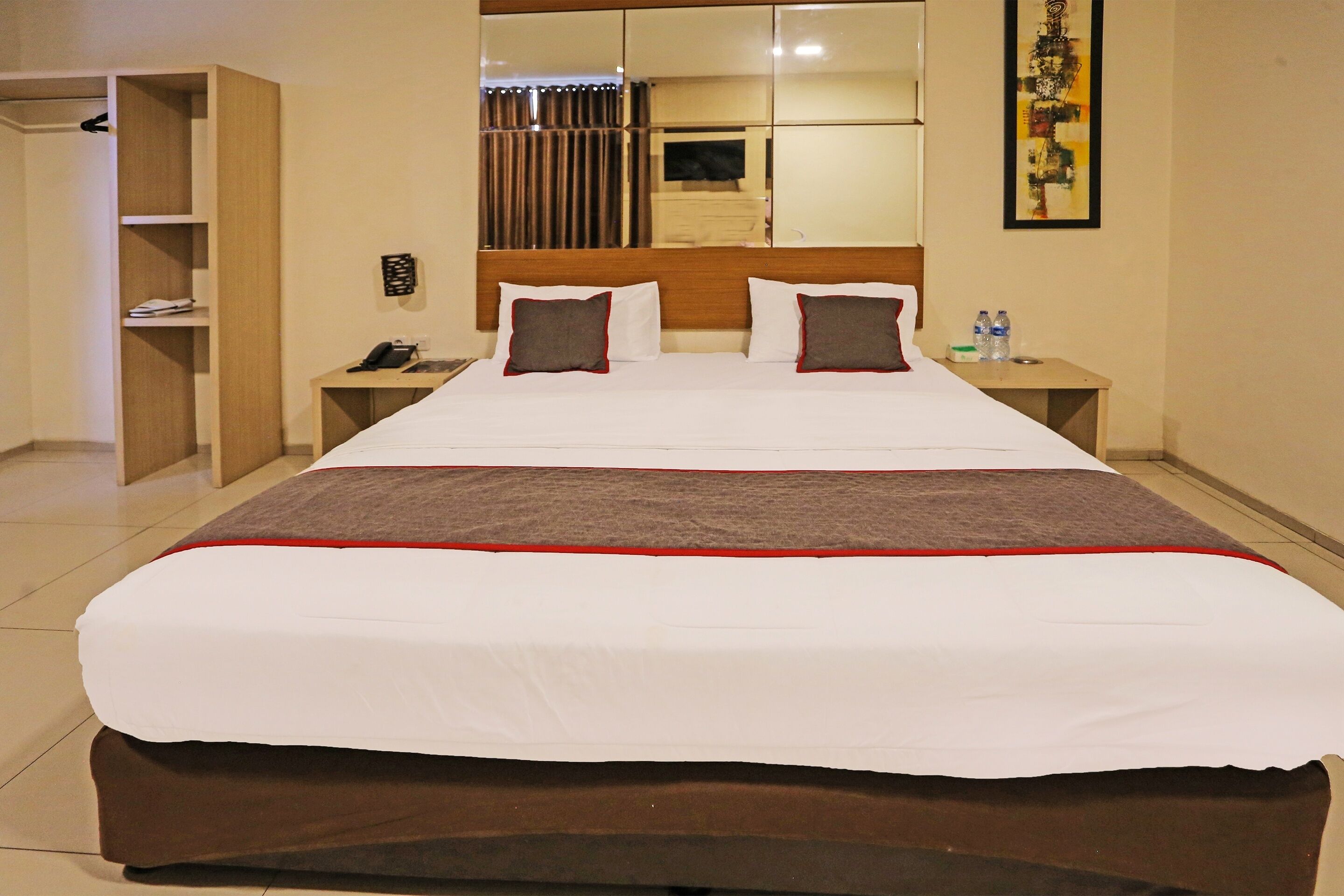 A hotel room with a large bed, two bedside tables, a wardrobe, and a mirror.
