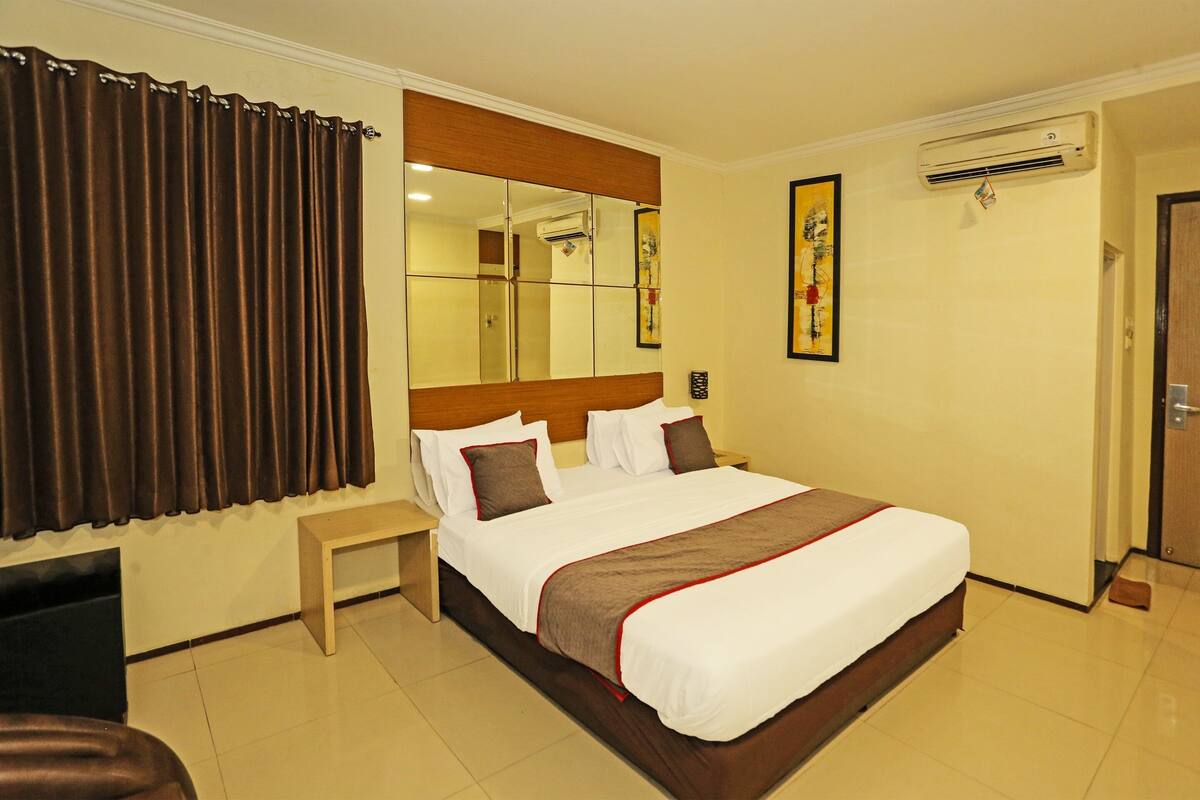 Une chambre d’hôtel avec un grand lit, une table de chevet, un miroir, un appareil de climatisation et une porte.