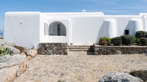 A white building with a stone pathway leading to a door with a circular window. - 360 Sunset Villa with Private Pool (Mykonos)