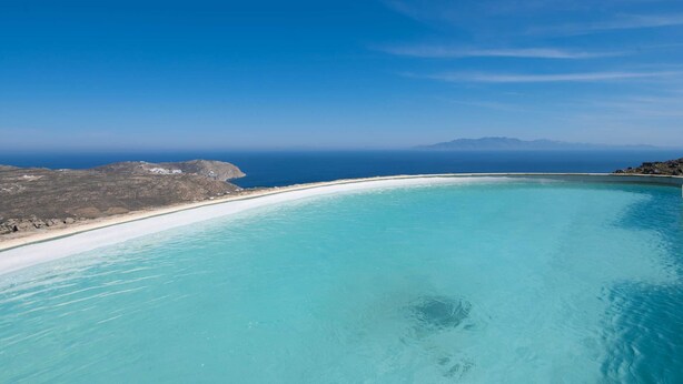 A coastal landscape with a clear blue sky, a sandy beach, and a calm turquoise sea. - 360 Sunset Villa with Private Pool (Mykonos)