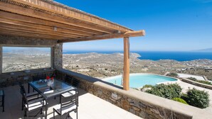 A terrace with a table and chairs, overlooking a coastal landscape with a pool. - 360 Sunset Villa with Private Pool (Mykonos)