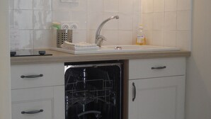 A compact kitchen with white cabinets, a built-in dishwasher, a sink, and a window above the sink. - Charming village house near Bédoin, at the foot of Mont Ventoux (Crillon-le-Brave)