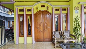 Un edificio de paredes amarillas con una puerta grande de madera, una mesa de cristal y un banco de bambú.