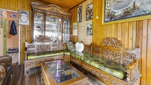 Una habitación de madera tradicional con muebles ornamentados, una mesa de centro con superficie de vidrio y un cuadro grande en la pared.