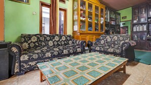 Una sala de estar con un conjunto de sofá, un aparador de madera con puertas de cristal y un camino de mesa estampado.