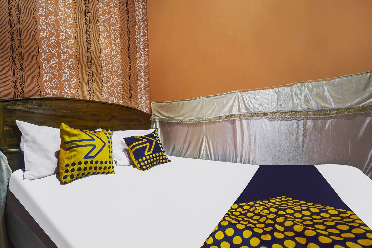 A bed with white and yellow pillows, a dark blue bedspread with yellow dots, and a wooden headboard.