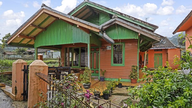 Una casa tradicional con techo verde y paredes de madera, rodeada de plantas en macetas y un portón de metal.