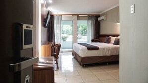 A hotel room with a bed, a desk, a chair, a television, and a sliding glass door leading to a balcony.