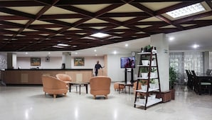 A spacious lobby with a reception desk, comfortable seating, a television, and a plant shelf.
