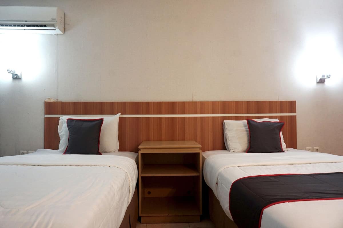 Ein Hotelzimmer mit zwei Betten, einem Holz-Kopfteil und einem kleinen Nachttisch dazwischen.