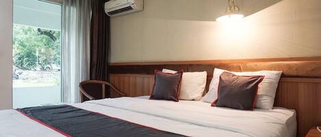 Quarto de hotel com uma cama grande, janela com cortinas, ar condicionado, abajur e cabeceira de madeira.