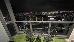 A balcony with a table and chairs, a potted plant, and a view of a cityscape at night. - Luxury 2B2B Well Furnished Spectacular View (Melbourne)