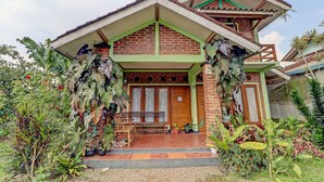 A two-story house with a green roof and brick walls, surrounded by lush tropical plants. - OYO Homes 90849 Cibeunying Homestay Cibodas Maribaya (Lembang)