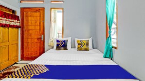 A bedroom with a bed, two pillows, a wooden door, a window with curtains, and a patterned rug. - OYO Homes 90849 Cibeunying Homestay Cibodas Maribaya (Lembang)