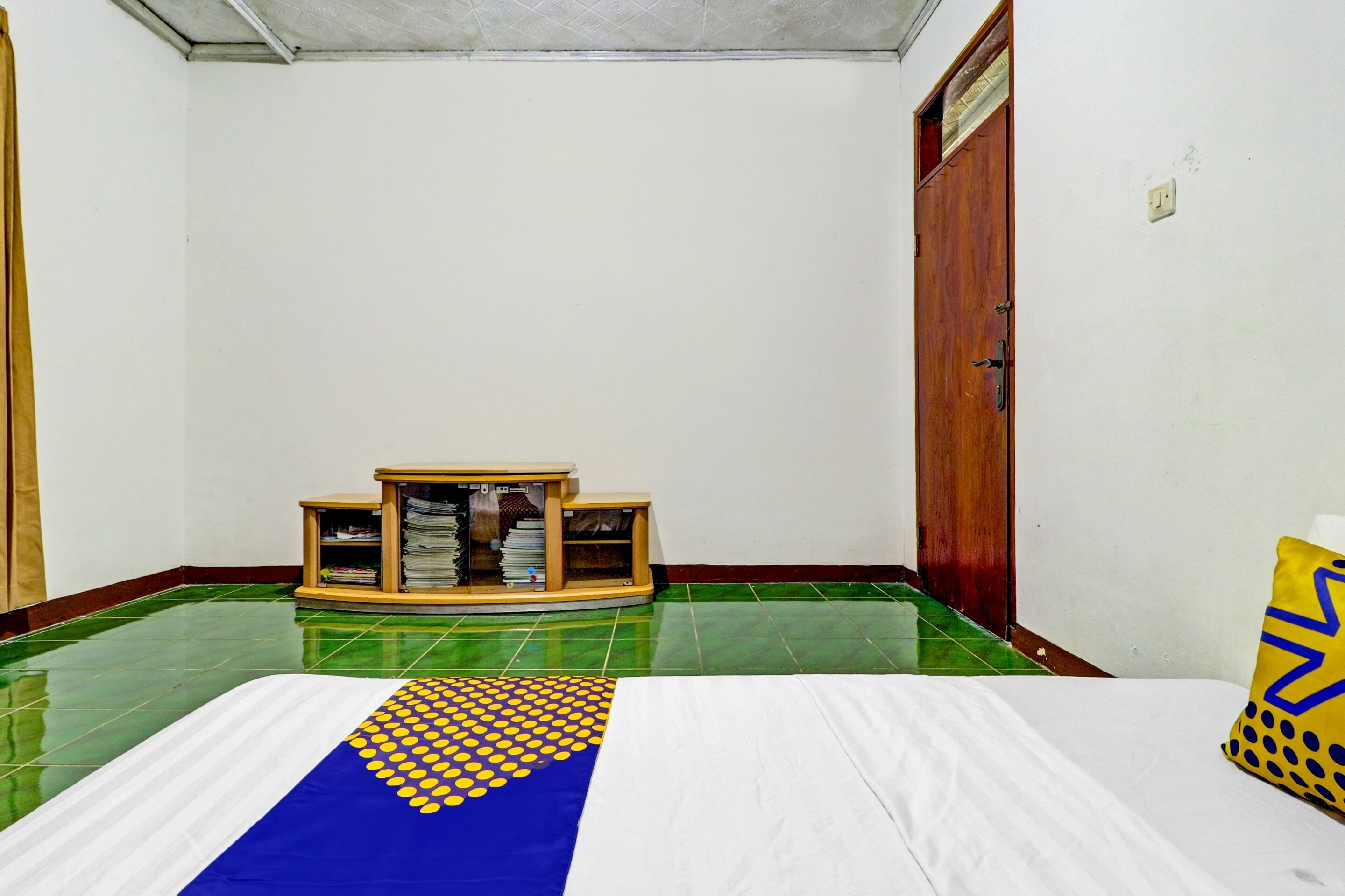 A room with a bed, a wooden cabinet, and a green tiled floor.