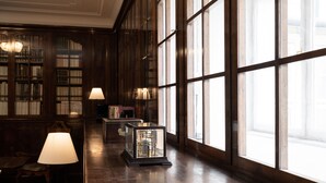 A library with wooden bookshelves, a long wooden table with lamps, and large windows.