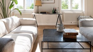 A spacious living room with a modern sofa set, a coffee table, and a large window providing natural light.