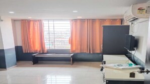 A hotel room with a bed, a desk, a chair, a TV, and a window with curtains. - Renuka Executive (Rajgurunagar)