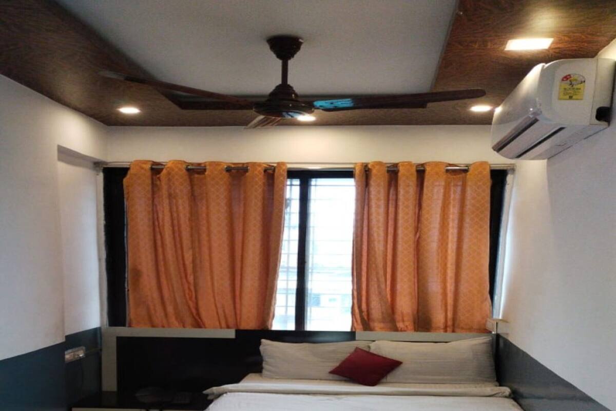 A bedroom with a bed, a ceiling fan, an air conditioning unit, and curtains.