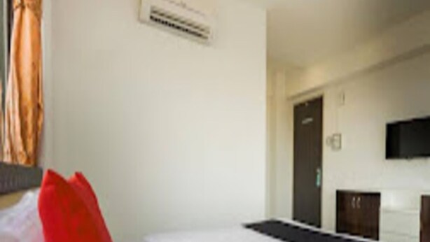 A hotel room with a bed, a television mounted on the wall, and a door leading to another room. - Renuka Executive (Rajgurunagar)