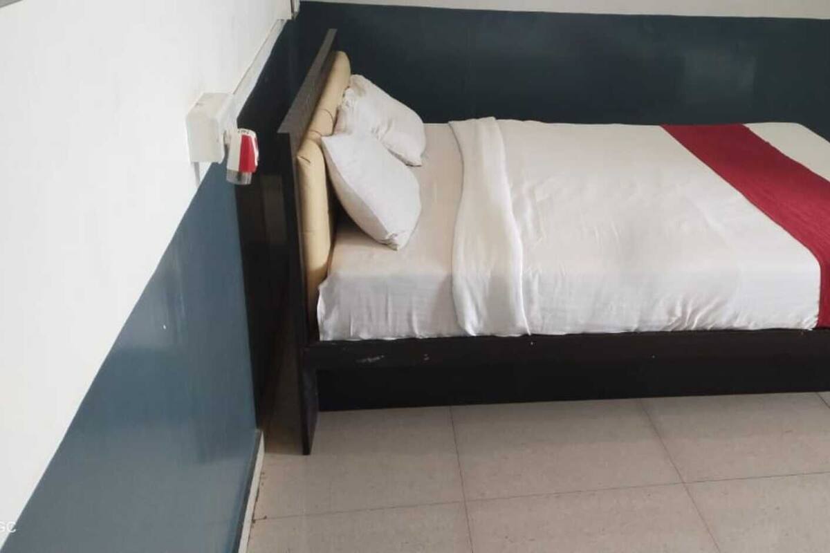 A bed with a white and red bedspread, a wooden headboard, and a nightstand with a lamp.