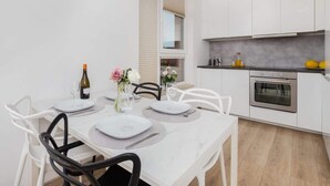 Una cocina moderna con armarios blancos, horno empotrado y comedor con mesa blanca dispuesta para cuatro personas.