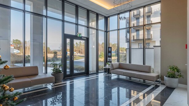 A modern lobby with large glass windows, a black-tiled floor, and two sofas. - Sunny Apartment with Parking | Near the Beach | Air Conditioning (Świnoujście)