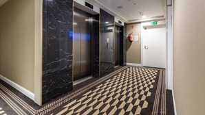 A modern hallway with marble walls, black and beige patterned carpet, and two elevators. - Sunny Apartment with Parking | Near the Beach | Air Conditioning (Świnoujście)