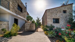 Un étroit sentier de pierre bordé de deux bâtiments en pierre dotés de fenêtres et d’un petit jardin fleuri.