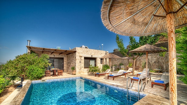 Une piscine entourée de murs de pierre et de verdure, avec des chaises longues et des parasols.