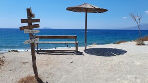 Une plage avec un banc en bois, un panneau indicateur et un parasol en chaume.