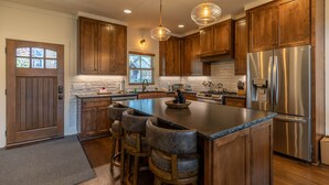 A modern kitchen with wooden cabinets, stainless steel appliances, and a central island with bar stools. - Woof Lodge at SweetGrass - pet friendly, outdoor fireplace, walk to lake (Blowing Rock)