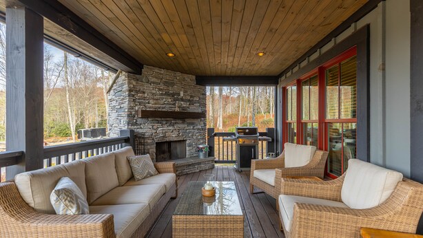 A covered outdoor seating area with wicker furniture, a stone fireplace, and a grill. - Woof Lodge at SweetGrass - pet friendly, outdoor fireplace, walk to lake (Blowing Rock)