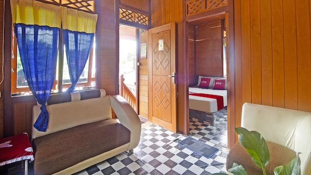 A room with a checkered floor, a sofa, a bed with red pillows, and a wooden door with a decorative lattice.