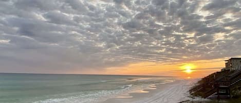 A beach with a sunset, a staircase leading to a building, and a sandy shore.