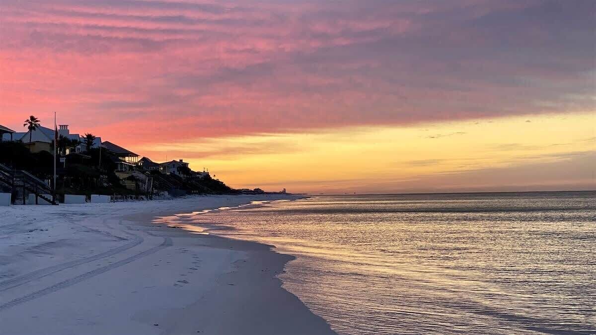 A beach with a sunset, sandy shore, and buildings in the background.