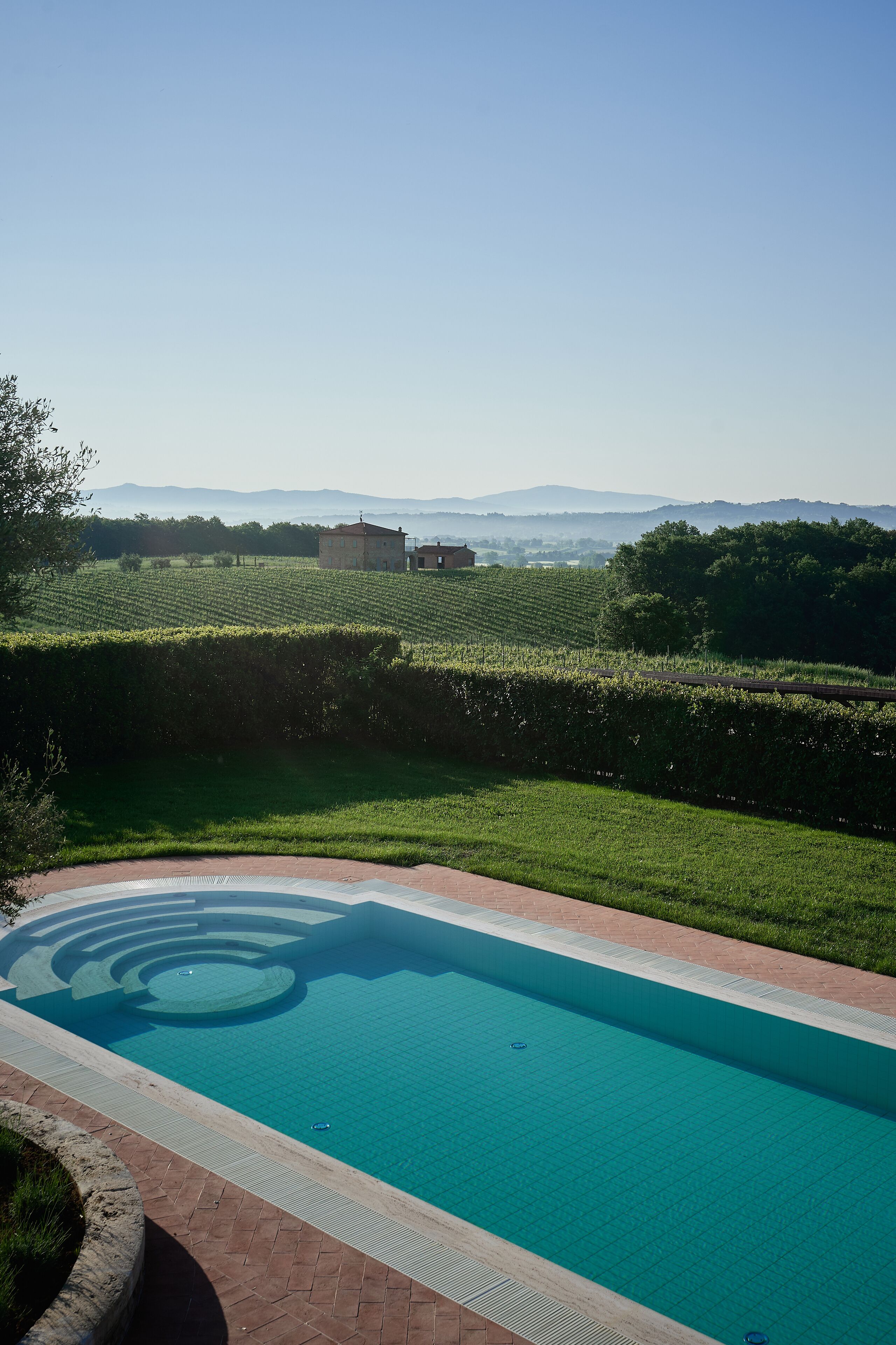 A swimming pool with a clear blue water surface, surrounded by a brick pathway and a well-maintained grassy area.
