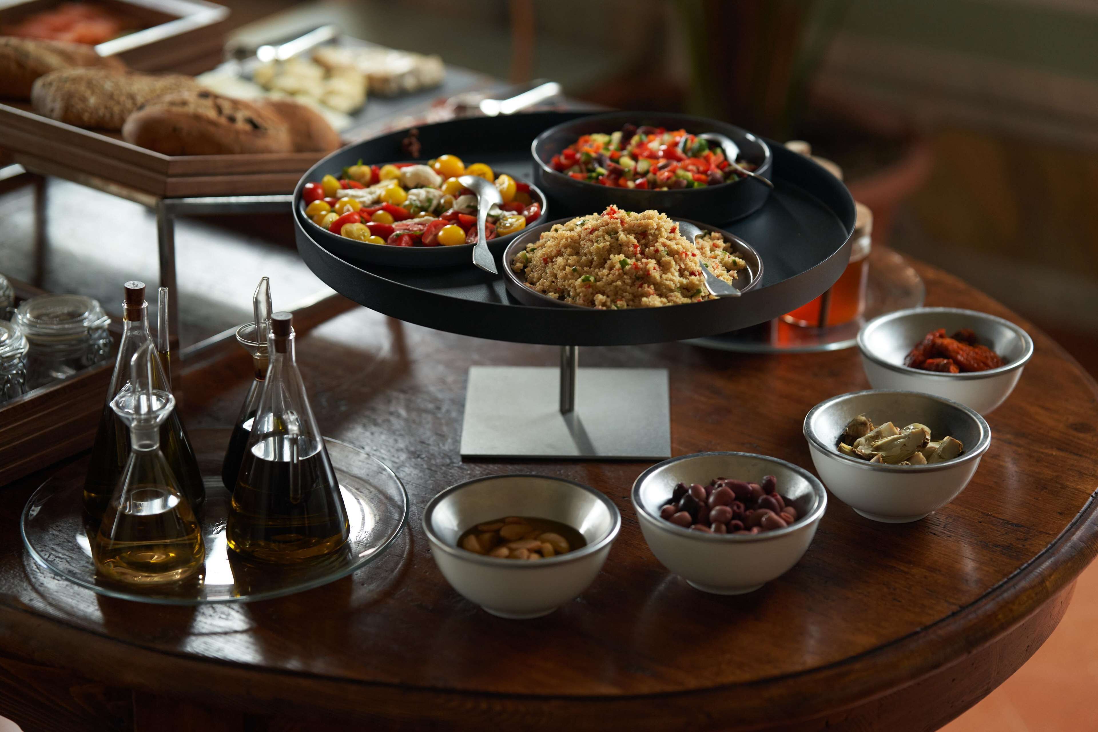 Una mesa de buffet con diversos platos, entre ellos ensaladas, cereales y legumbres, además de salsas y botellas de aceite de oliva.