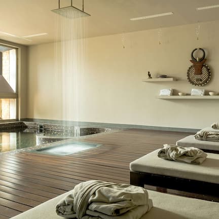 A spa room with a wooden floor, a hot tub, and two massage beds with towels.