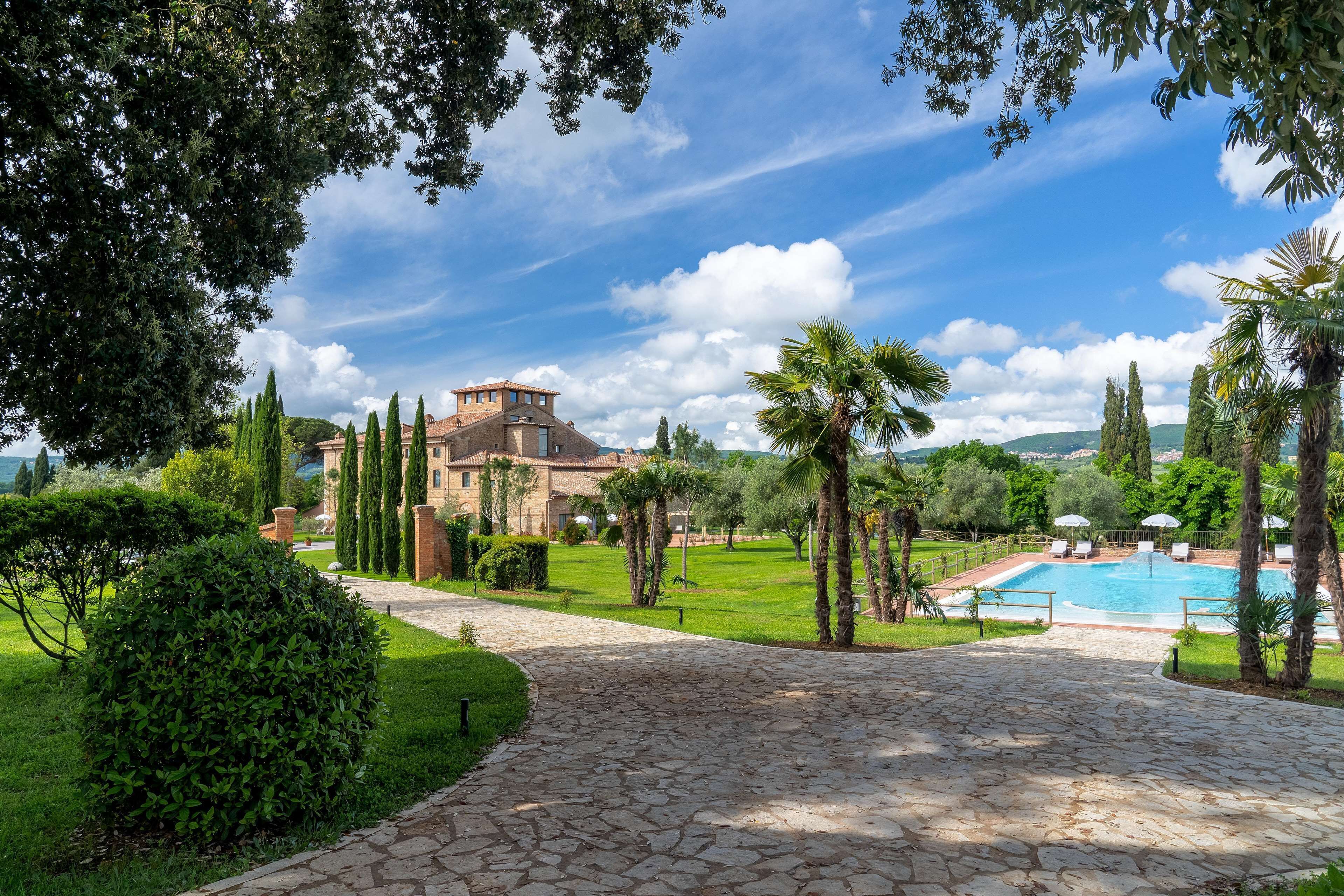 A stone pathway leading to a pool area with palm trees and a large building in the background.