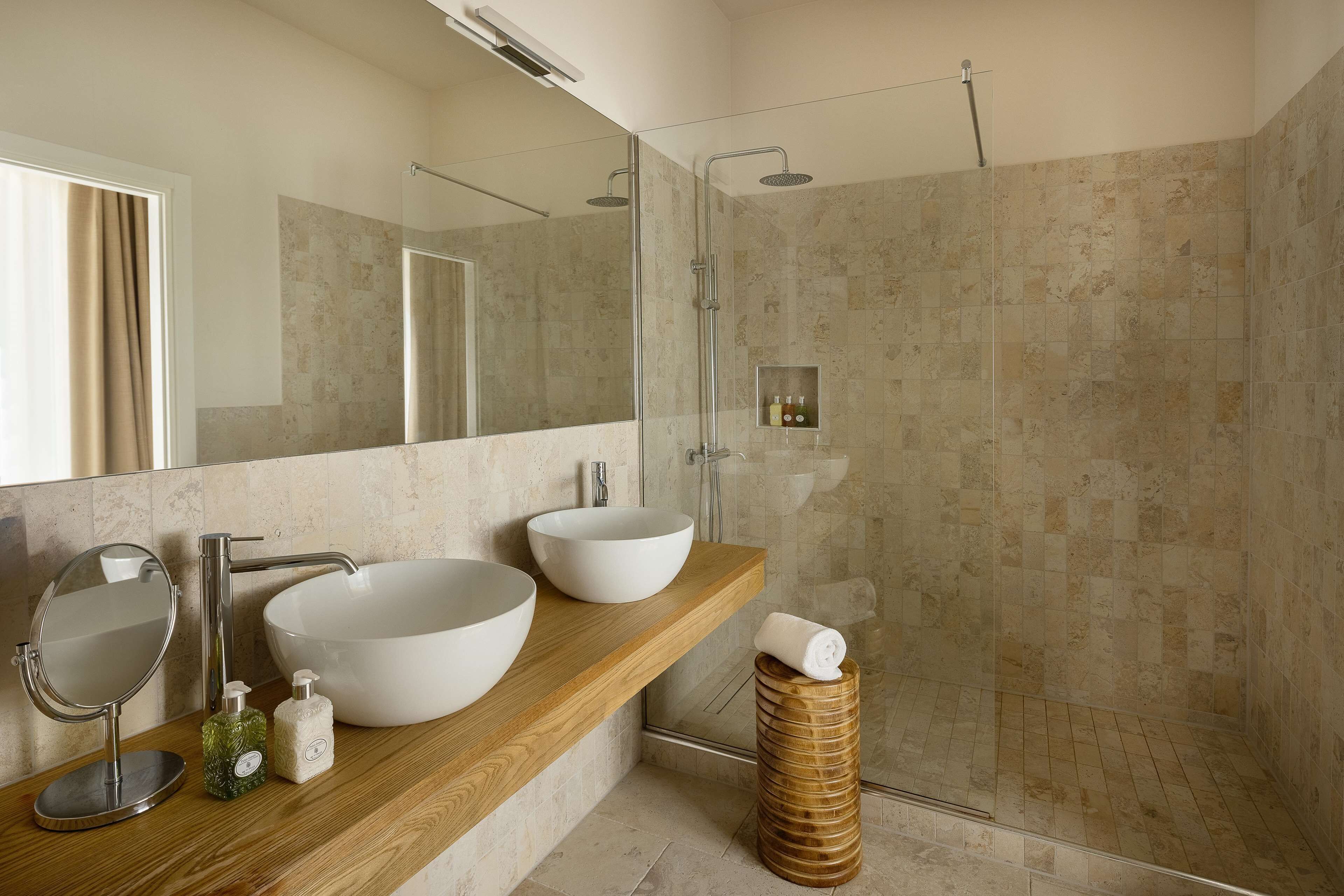 A modern bathroom with two large white sinks, a round mirror, and a wooden vanity.