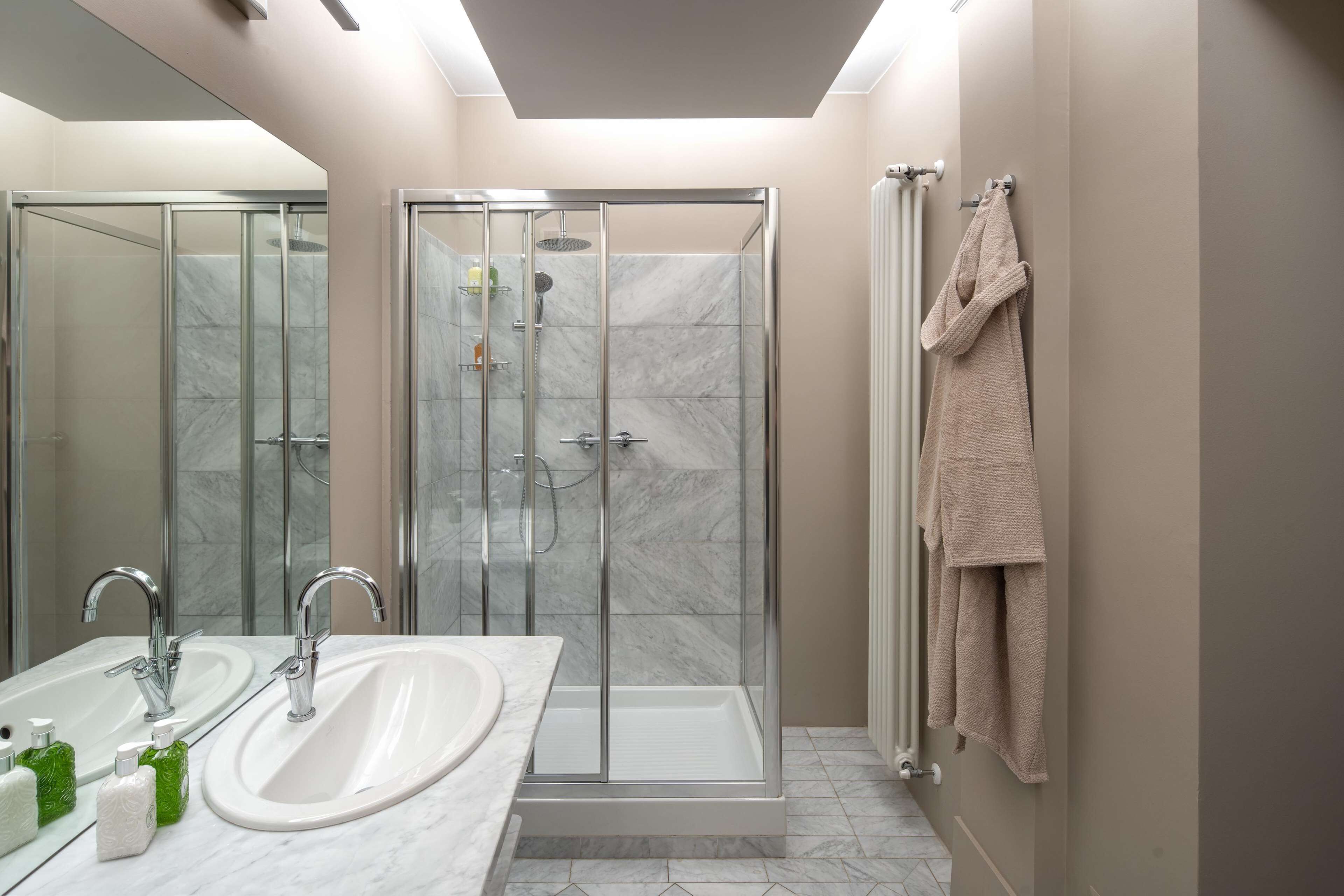 A modern bathroom with a glass-enclosed shower, a white sink, and a large mirror.
