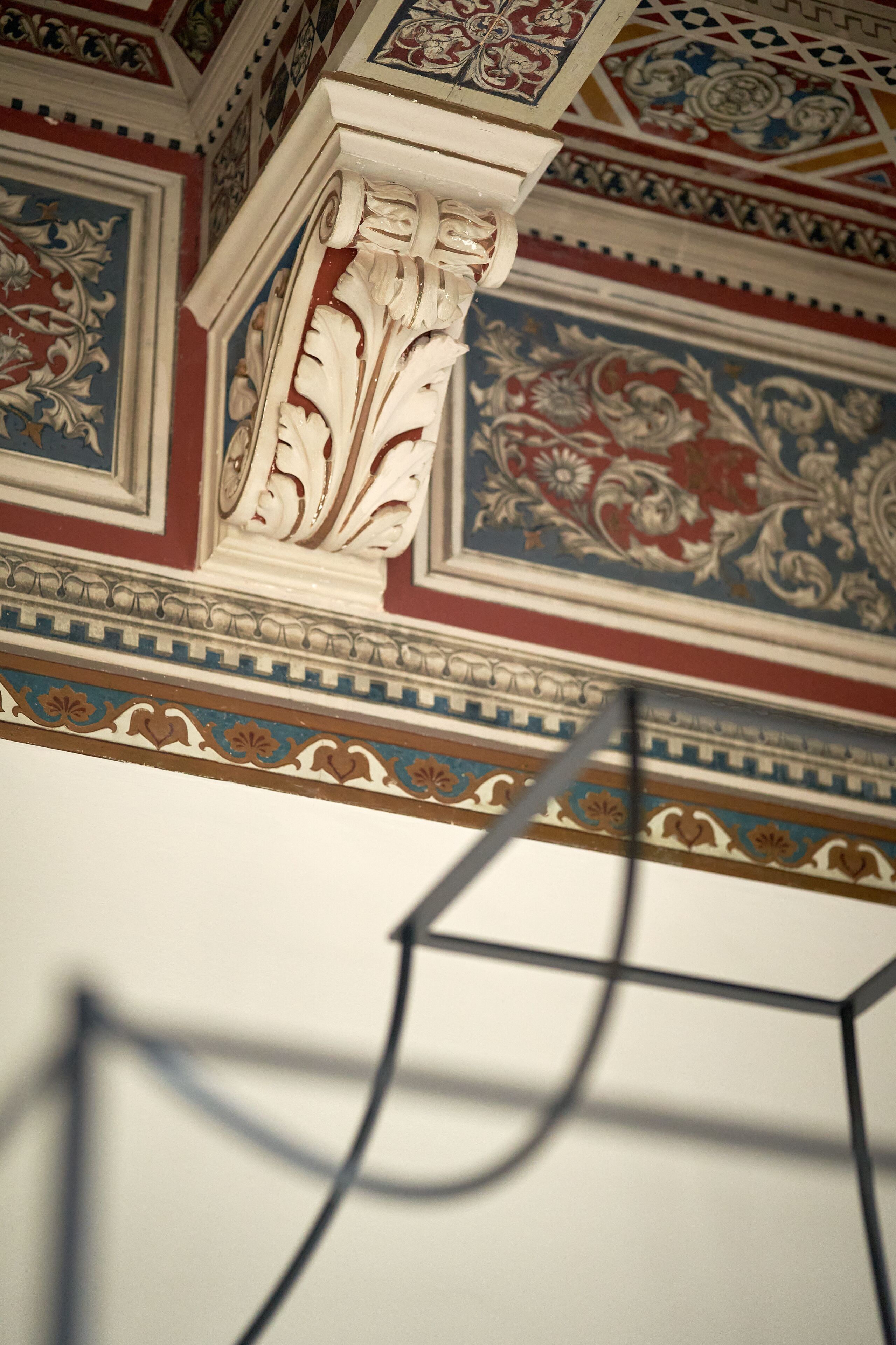 Un plafond orné de motifs floraux et géométriques, une colonne blanche et une structure métallique moderne.