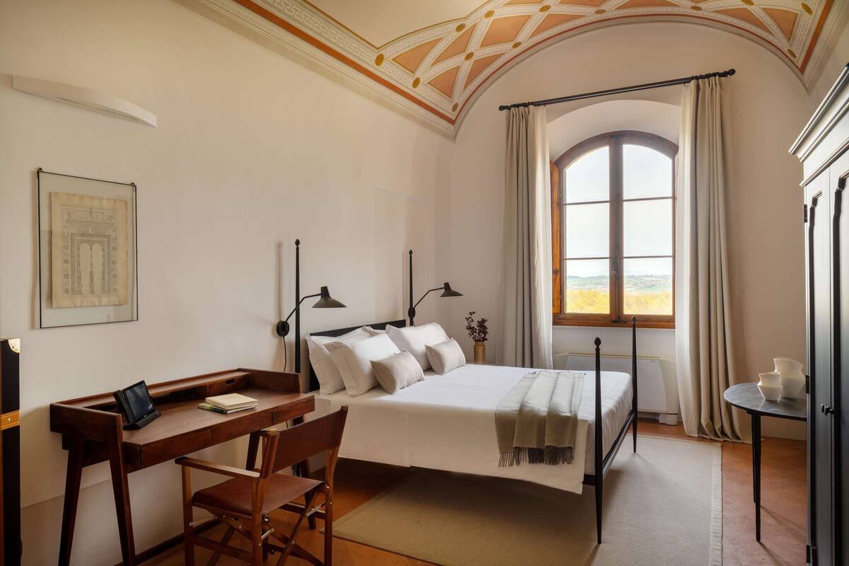 Ein Schlafzimmer mit Bett, Schreibtisch, Stuhl und einem großen Fenster mit Vorhängen.