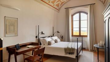Un dormitorio con cama, escritorio, silla y un ventanal con cortinas.