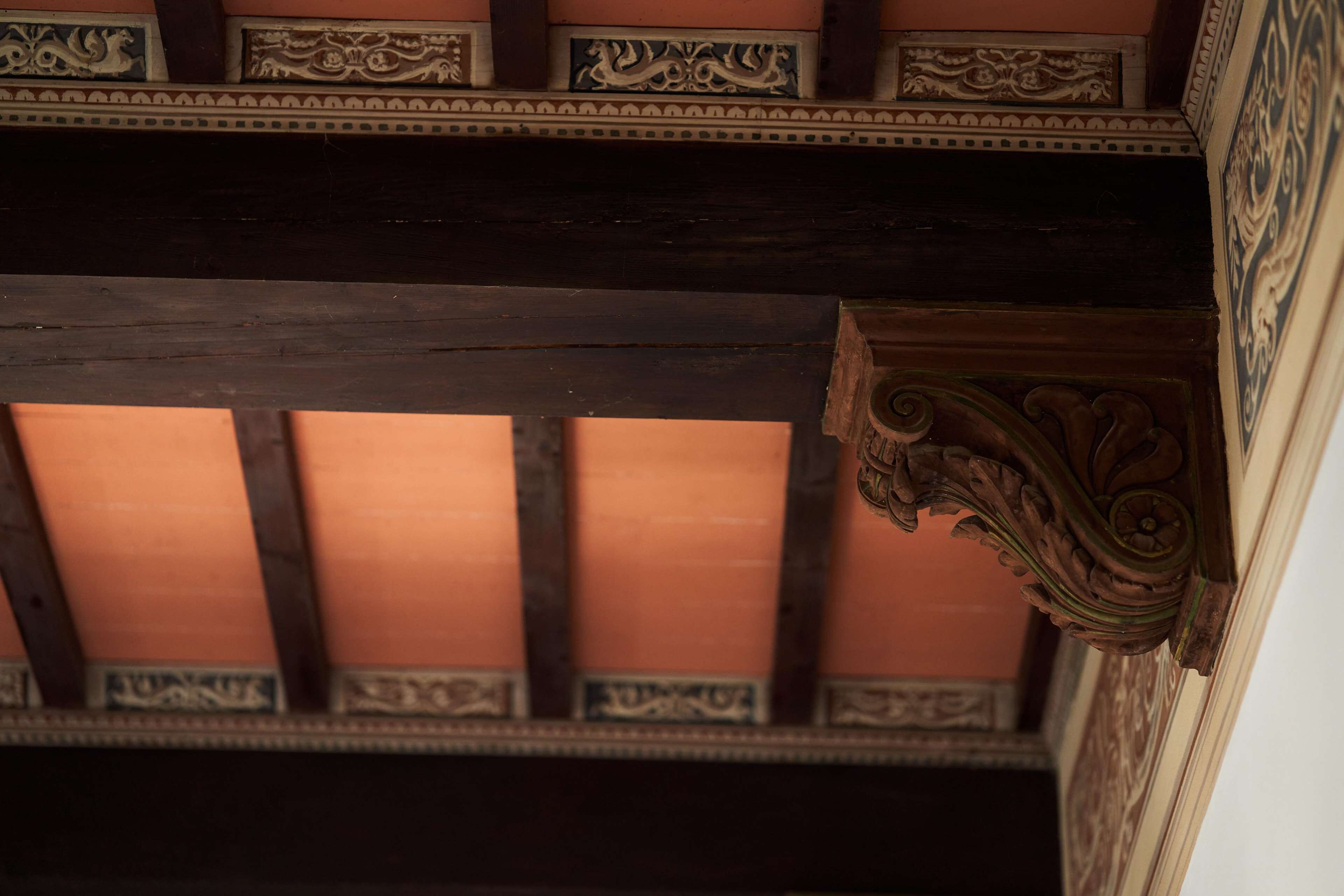 Een plafond met versierde houten balken en decoratieve lijsten.