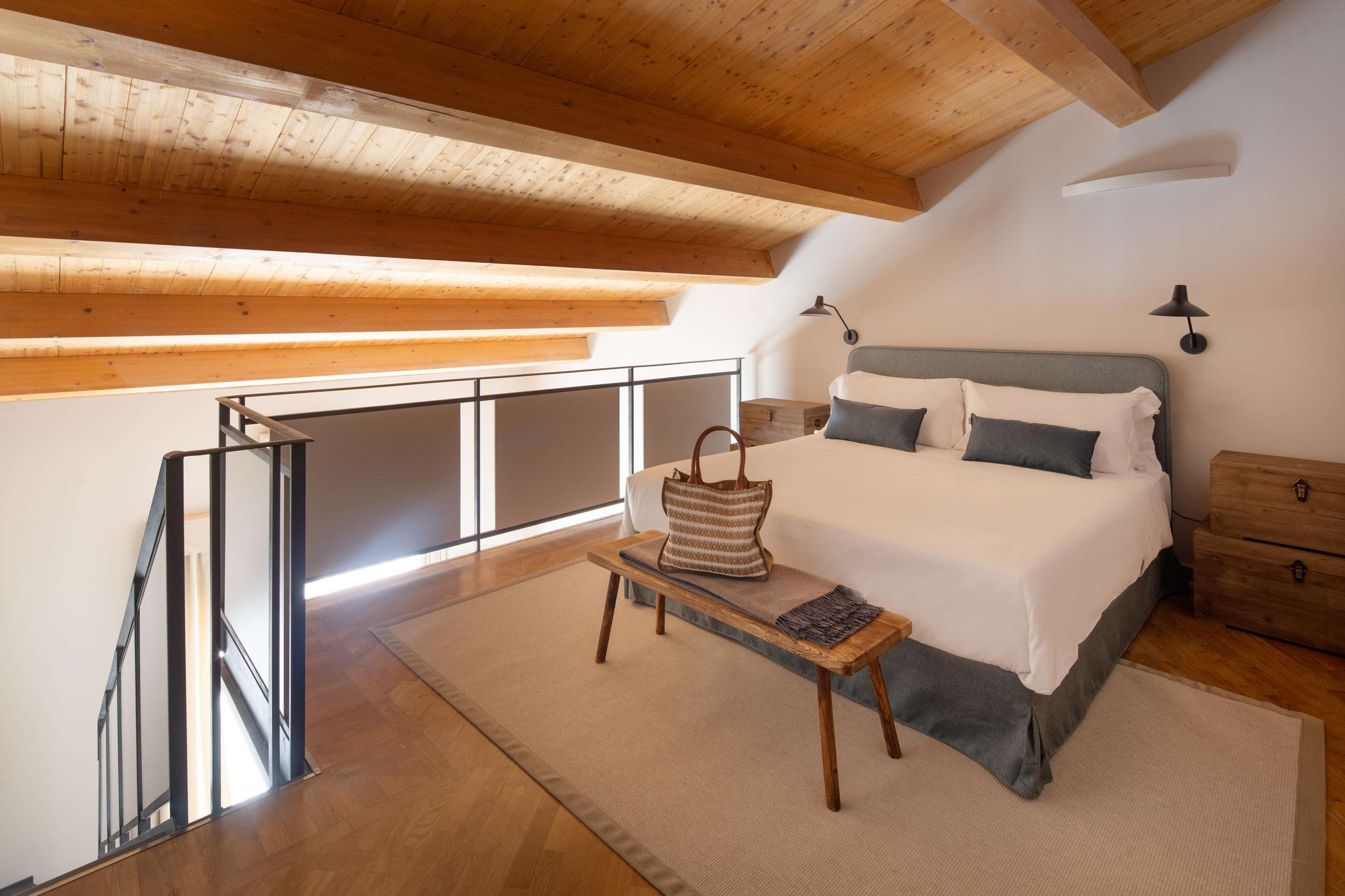 A bedroom with a bed, bedside table, lamp, and a wooden chest of drawers.