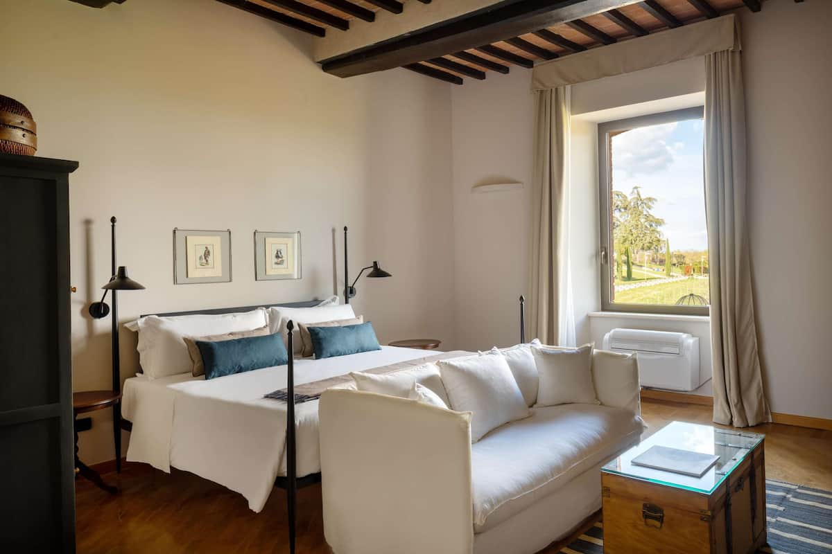 Ein Schlafzimmer mit einem Bett, einem weißen Sofa, einem Glastisch und einem Fenster mit Vorhängen.