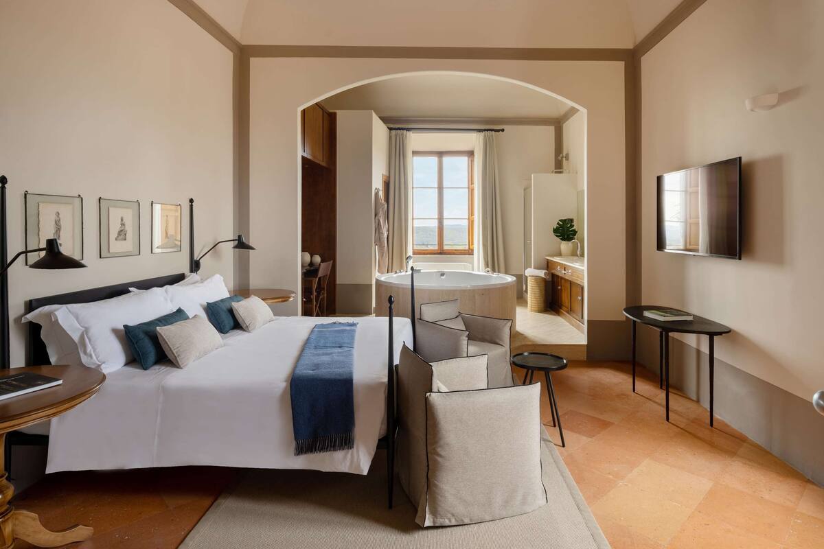 Ein Hotelzimmer mit einem großen Bett, einer Sitzecke mit Blick, einem runden Tisch, einem Fernseher und einem Badezimmer mit Badewanne und Waschbecken.